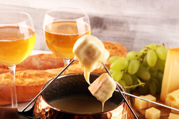 Obraz premium Gourmet Swiss fondue dinner on a winter evening with assorted cheeses on a board alongside a heated pot of cheese fondue with two forks dipping