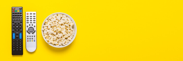 Two remotes from the TV, TV tuner and a bowl of popcorn on a yellow background. Concept series, film, sports. Banner. Flat lay, top view