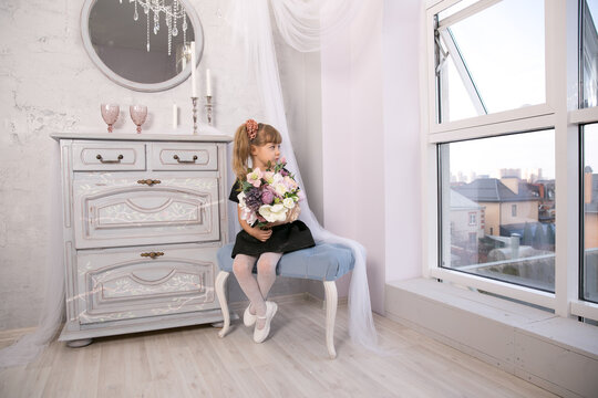 Pretty little girl holding a bunch of colouful flowers in her hands against a backdrop of closed curtains with copyspace