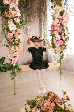 Cute little girl on swings decorated with flowers on the background of the house and smiling