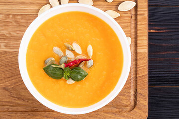 Pumpkin and carrot soup with cream and pumpkin seeds on wooden background with copy space. Top view