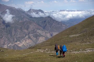 Obraz premium Backpackers trekking in mountains. Tourists hike through the valley. Valley near Bulungu village.