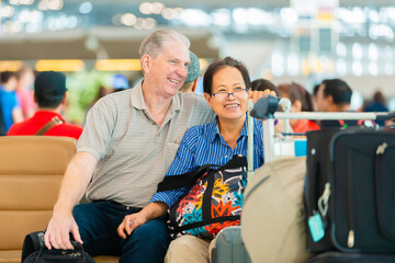 Happy Senior couple is sitting at airport terminal. They are embracing and smiling.