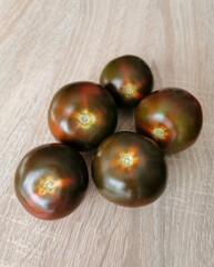Five fresh, dark red heirloom tomatoes on a wooden table.