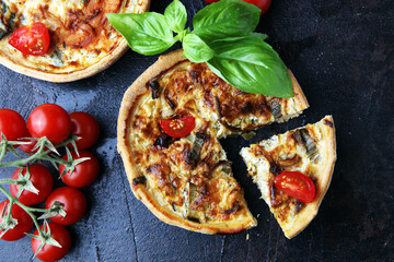 Savory mini quiches or tarts on a rustic board. Flaky dough pies. Fresh basil and tomatoes on...