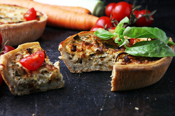 Savory mini quiches or tarts on a rustic board. Flaky dough pies. Fresh basil and tomatoes on handmade quiche