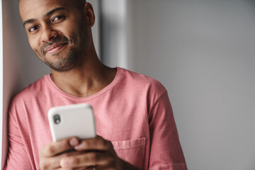 Image of smiling african american guy using mobile phone