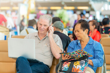 Modern approach. Senior man with laptop talking on cellphone and Senior woman holding tablet while sitting happily together at the airport.