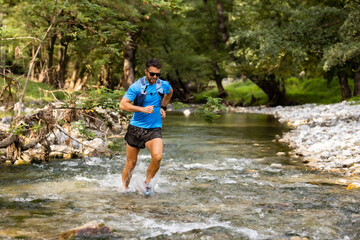 Young man in sports equipment running in mountain river 