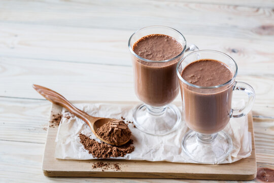 Coffee latte macchiato or hot chocolate in two glasses on wooden background, a spoon with cocoa powder. Selective focus, copyspace