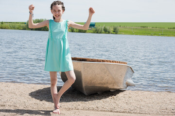 Nice girl with dreadlocks on her head in summer dress on the lake by the iron boat.