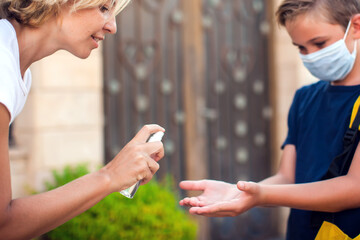 Mother and kid with medical mask disinfecting hands with sanitizer outdoors. Life during coronavirus pandemic.