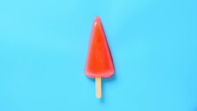 top view watermelon slice shape and flavor popsicle melting on a blue background timelapse