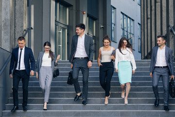 Confident team members walking on stairs. Business men and women in formal suits go and talk on the background of modern office building