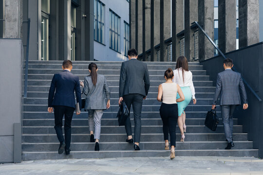 Young business people colleagues returning from their break. Men and women in formal suits going up stairs into office building. Partnership, communication business people concept.