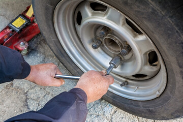 a man removes an old worn out wheel from his car to replace it with a new one