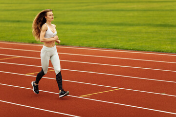Athletic woman running at the stadium, working out, keep herself in shape, wearing sportswear, white top and pants, recommends doing sports, healthy lifestyle concept