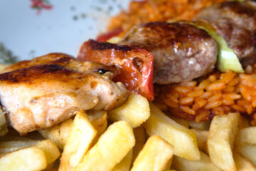 Delicious dish from Bosnian cuisine - mixed meat skewers served with french fries, grilled vegetables and rice with paprika 