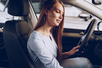 Attractive young woman sitting in new car in showroom