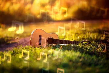background with musical wooden guitar lying in green grass and brilliant notes sounds fly over it