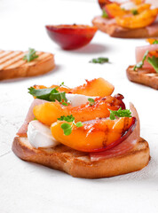 Bruschetta with grilled peaches, prosciutto and mozzarella topped with parsley and cilantro on the white table