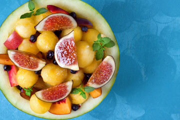Fruit salad with yellow watermelon, fig, nectarine, plum, bilberry, apple, banana and honey in the watermelon half on the blue table