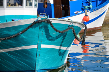 Closeup of turquoise and blue colored fishing boats in the harbor of the community of Port-en-Bessin-Huppain in Normandy, France, coast of English Channel, a sunny day in summer, reflections in water