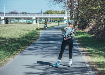 Photo from the back, of a girl, sporty, skating with in-line skates.