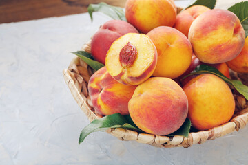 Ripe peaches in a wicker basket on a stone gray table with a juicy peach slice with a stone pit.