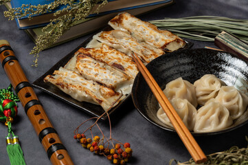 Material of traditional chinese fried dumplings(also called gyoza,pot sticker) on table with black background and decorate with chinese style fans and tea cup.