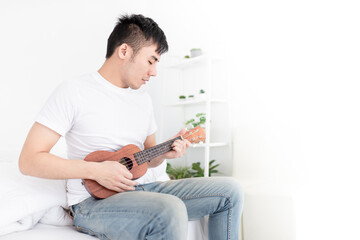 asian man artist holding and playing ukulele in his bedroom, he training to show acoustic concert, happiness activity