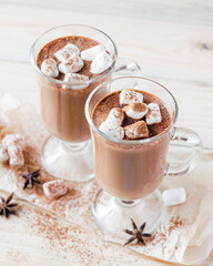Two portions of hot chocolate with mini marshmellow in glasses on a rustic wooden background. Vertical orientation, copyspace
