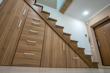 Modern architecture interior with luxury hallway with glossy wooden stairs in multi-storey house. Custom built pullout cabinets on glides in slots under stairs. Use of space for storage.