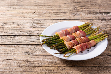 Green asparagus wrapped with bacon on wooden table. Copy space