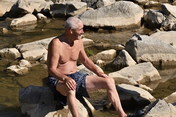 A man sits on river stones in the sun