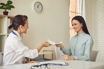 Young smiling doctor giving paper prescription to woman patient in medical clinic