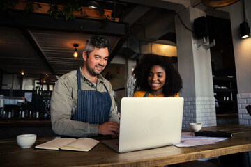 Male and mixed race female coffee shop owners smiling at laptop in coffee shop. - Powered by Adobe
