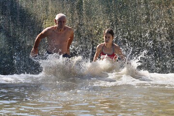 Older man and a girl slide on dam down the river