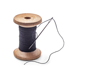 Black thread on an old wooden spool and a sewing needle.