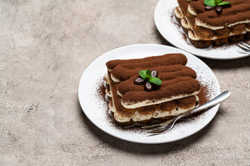 Two portions of Classic tiramisu dessert on ceramic plate on concrete background