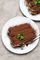 Two portions of Classic tiramisu dessert on ceramic plate on concrete background