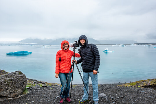 Blue glacier icebergs in lagoon lake in Iceland with photographer photography couple man woman landscape view on cloudy day with ice floating on water and turquoise color