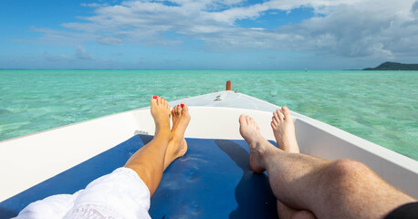 Man and woman relaxing as couple on the bow of a boat over beautiful tropical island turquoise water