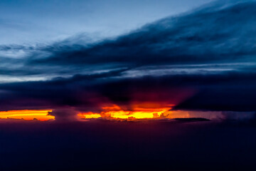 Colorful dramatic red dark sunset sun rays behind clouds in Virginia horizon high angle aerial view from airplane window from Dulles airport with skyscape