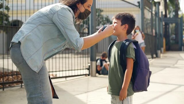 Caucasian woman straightens the protective mask on her son. They kiss on their masks and greet each other. Elementary student's first day of school during coronavirus pandemic. Concept back to school.