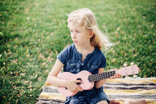 Pensive Blonde Girl Playing Pink Guitar Toy Outdoor. Child Playing Music And Singing Song In Park. Hobby Activity For Children Kids. Authentic Candid Childhood Moments.