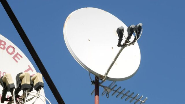 Satellite parabolic dish and signal receivers. TV antenna on wall of house. Yagi directional TV antenna. Signal amplifier. Hot sunny day. Blue sky. Broadcast reception concept. Residential building