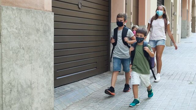 Four children walking down the street, going to school. It's the first day of school during coronavirus pandemic. They wear protective face masks and backpacks. Concept back to school on COVID-19.