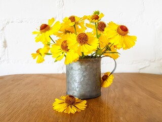 Yellow rudbekia flowers or coneflowers in an iron cup on a wooden table on a white background.