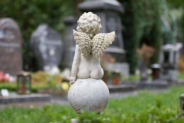 a little angel is sitting on a ball on a cemetery in front of graves in the blurred background